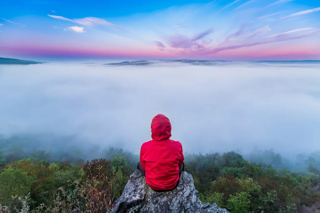 Person sitting alone on a rock at a foggy sunrise representing grief New Day Therapies Hull